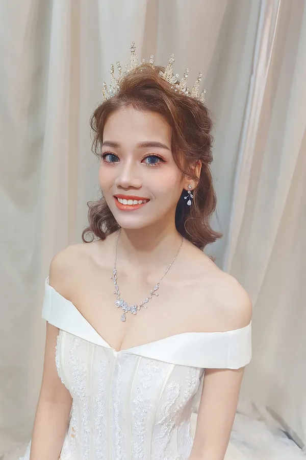 Smiling bride with crystal crown and off-shoulder gown, soft glam makeup by THEENG, Kuantan