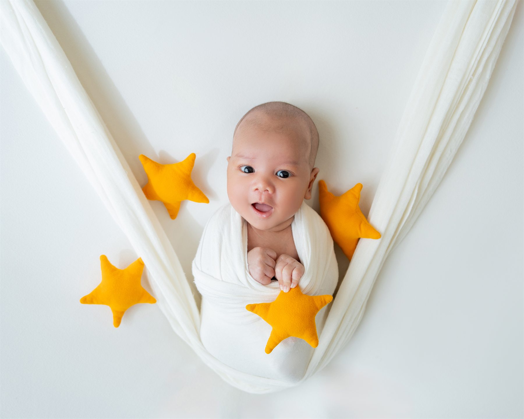 Newborn photography by Famous Bridal, baby wrapped in white hammock with yellow stars
