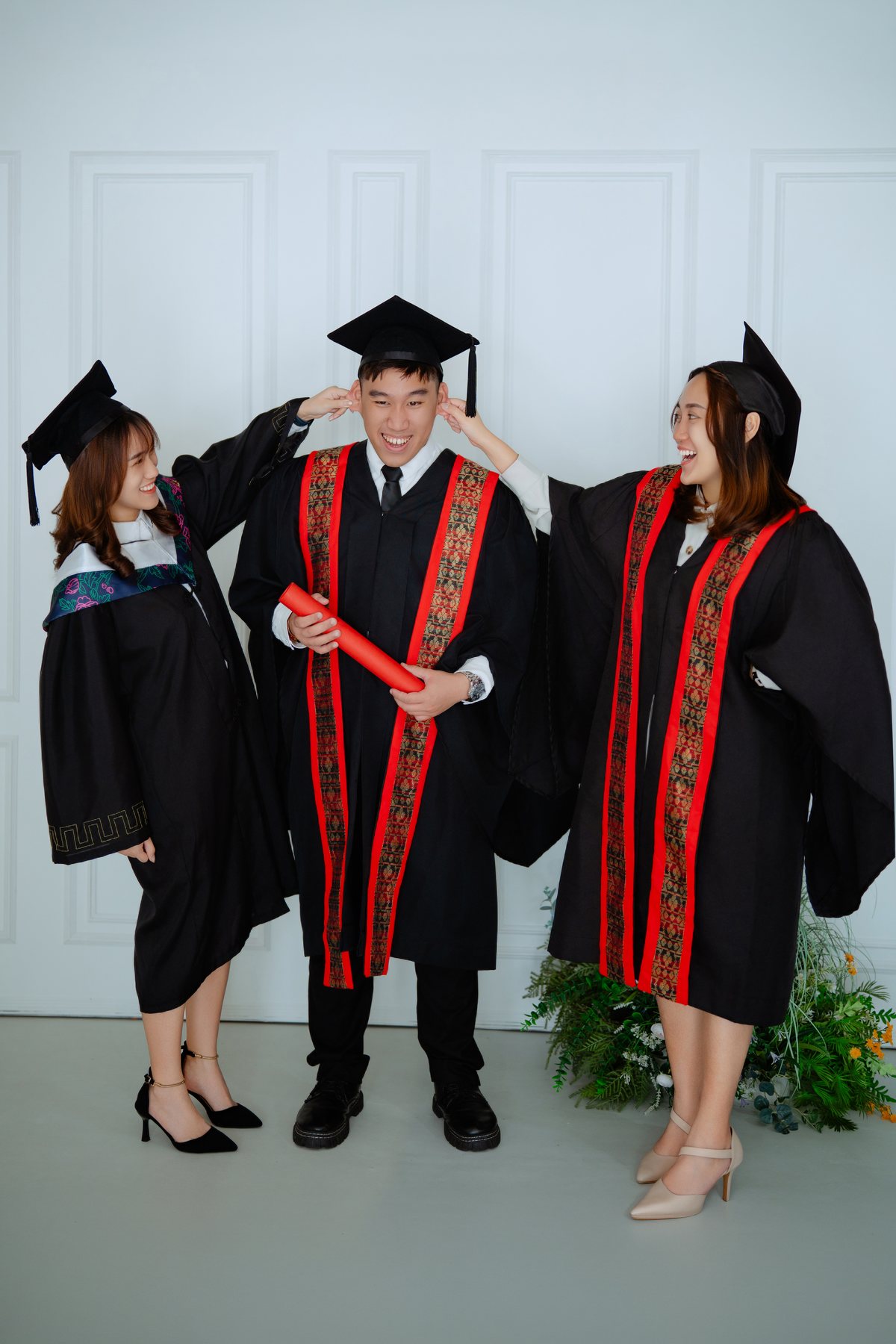 Three graduates in convocation robes with diploma scrolls