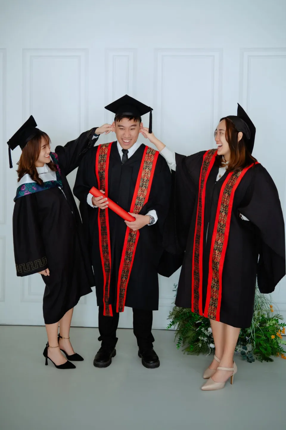 Three graduates in convocation robes with diploma scrolls